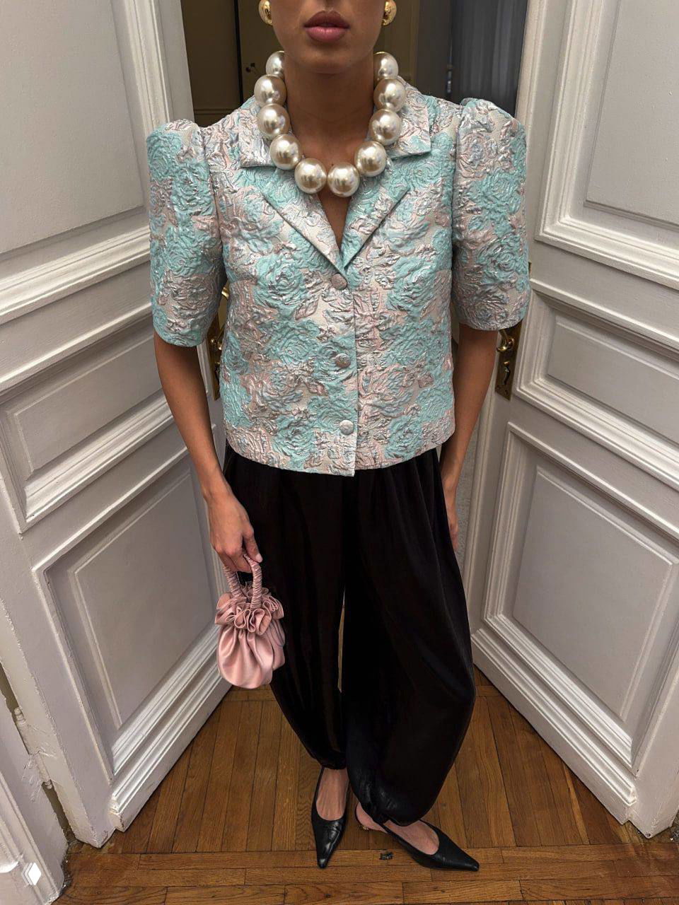 Короткий мятно‑розовый жакет из жаккарда с объёмным узором, крупное жемчужное ожерелье и стильные аксессуары — образ для выхода и вечерних мероприятий.