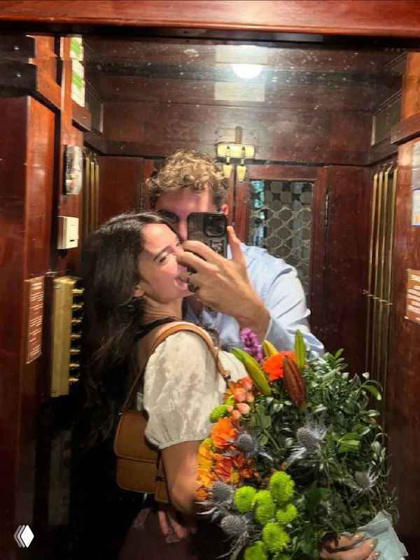 Зеркальное селфи пары в лифте: парень обнимает девушку, в кадре большой букет цветов и тёплая атмосферная обстановка.