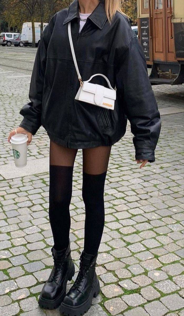 Образ с чёрной кожаной курткой, чёрными высокими гольфами и массивными ботинками на тротуаре — грубые ботинки и короткая юбка создают контраст.
