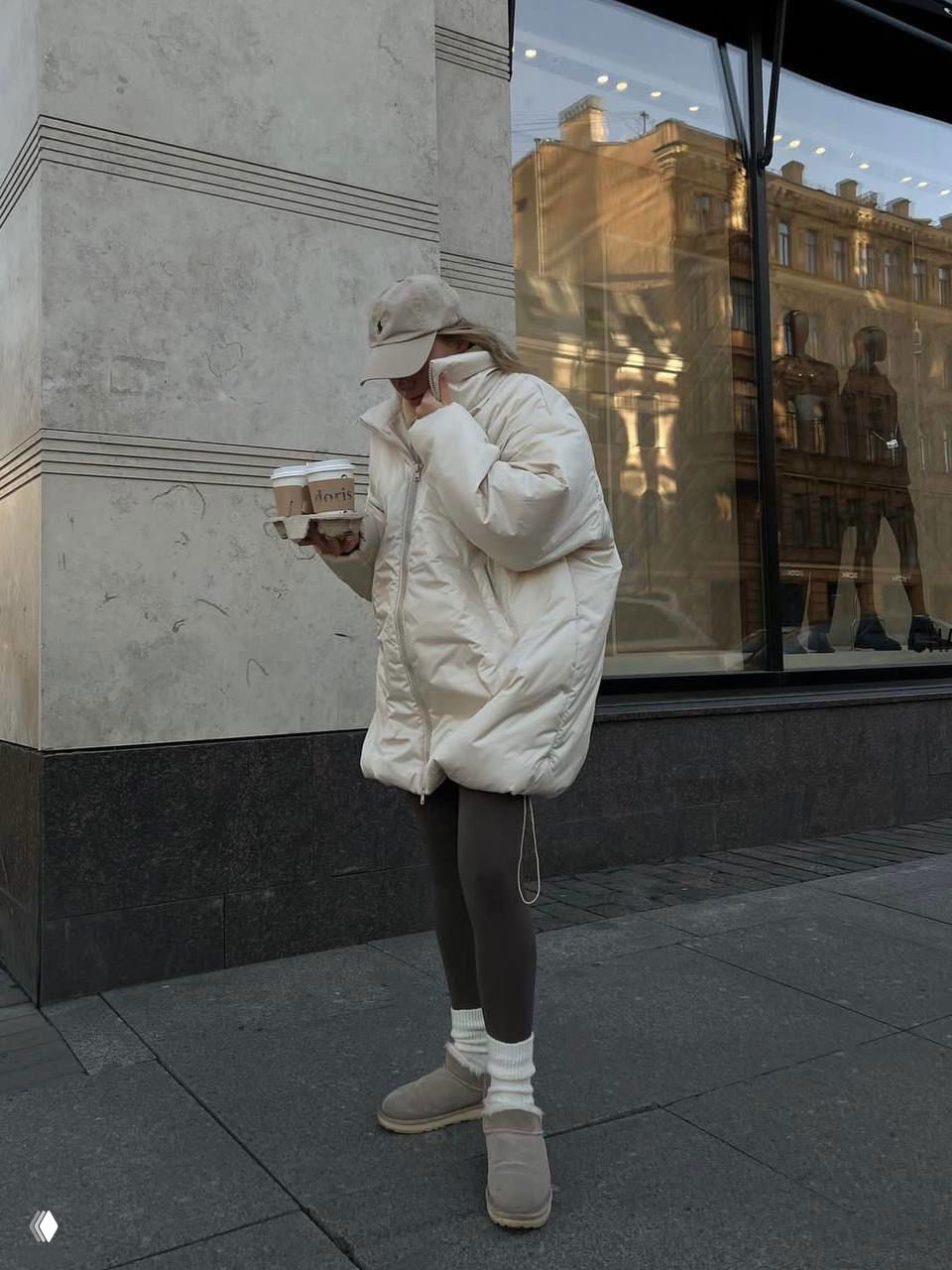Нейтральный образ: пуховик кремового цвета, тёмные леггинсы и белые гетры поверх обуви — спокойная палитра и функциональность для улицы.