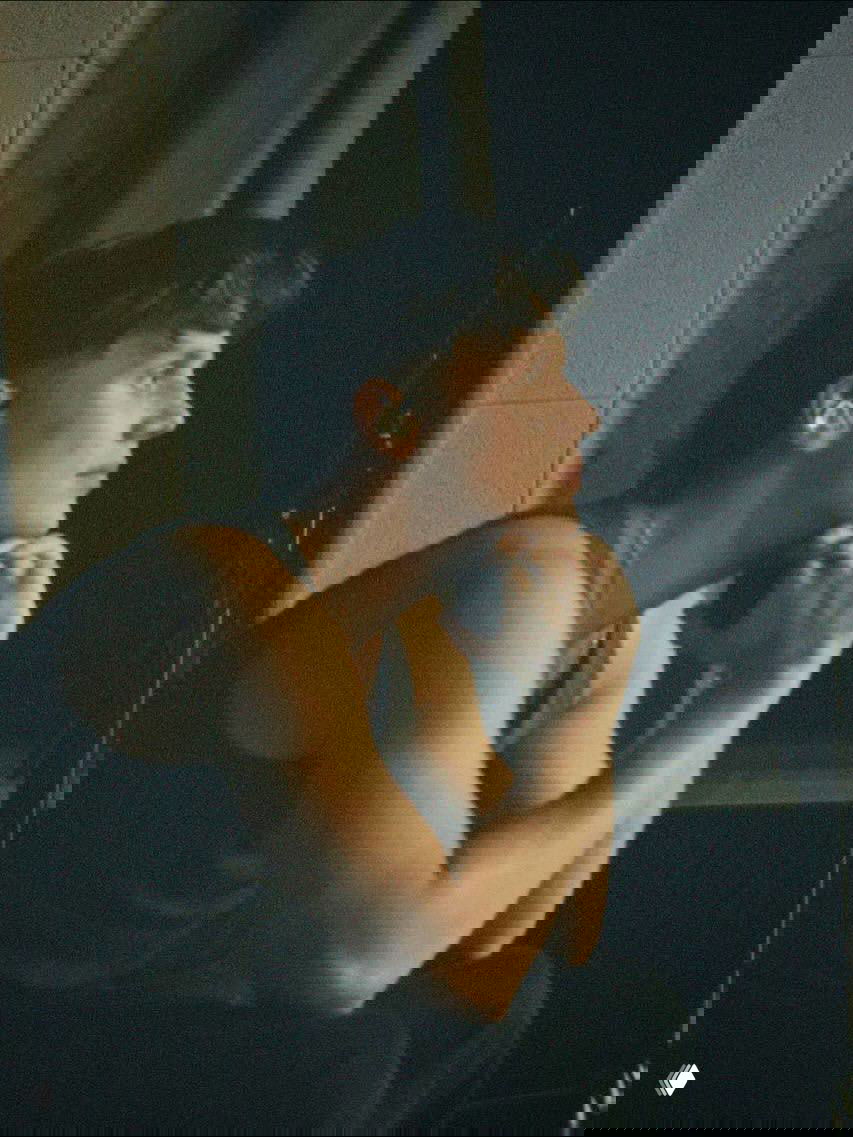 Портрет Вани Дмитриенко в профиль, задумчиво опирается подбородком на руки в закулисной обстановке, тёплое освещение и интимная атмосфера.