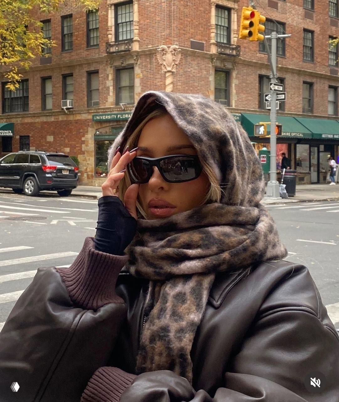 Женщина в больших солнцезащитных очках и тёплом шарфе на фоне городских улиц, крупный план, осенний уличный стиль.