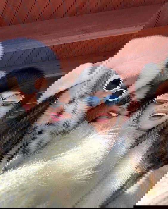 Групповое селфи: несколько девушек в тёплых шубах и пушистых шапках улыбаются на улице, зимняя атмосфера, солнечный свет.