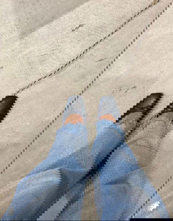 Ноги в чёрных балетках и джинсах стоящие на трещиноватом бетонном полу — минималистичный ракурс обуви для поездки.