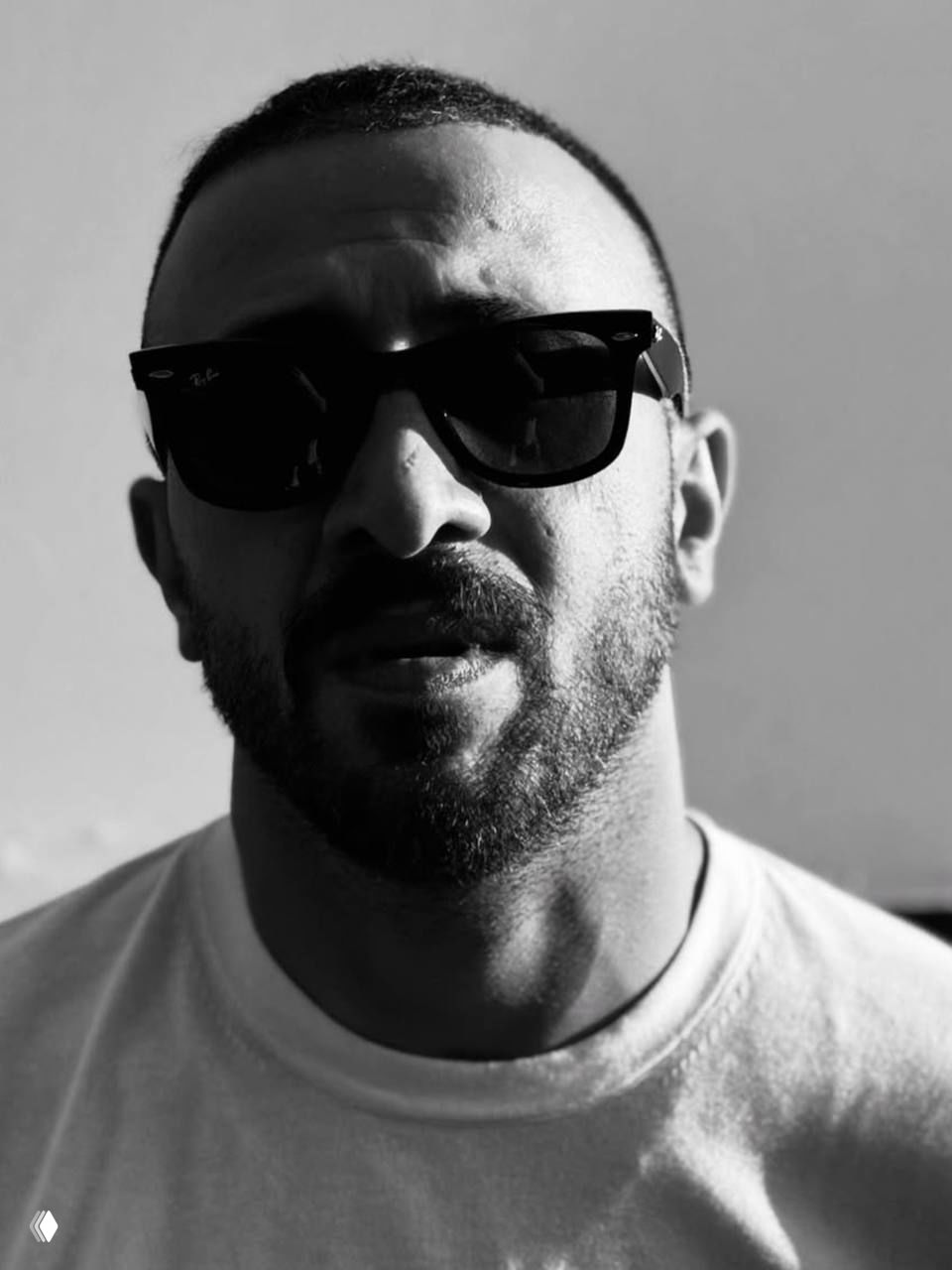 Чёрно-белый портрет мужчины в солнечных очках; сильный контраст света и тени, строгое выражение лица и эффект винтажной студийной съёмки.