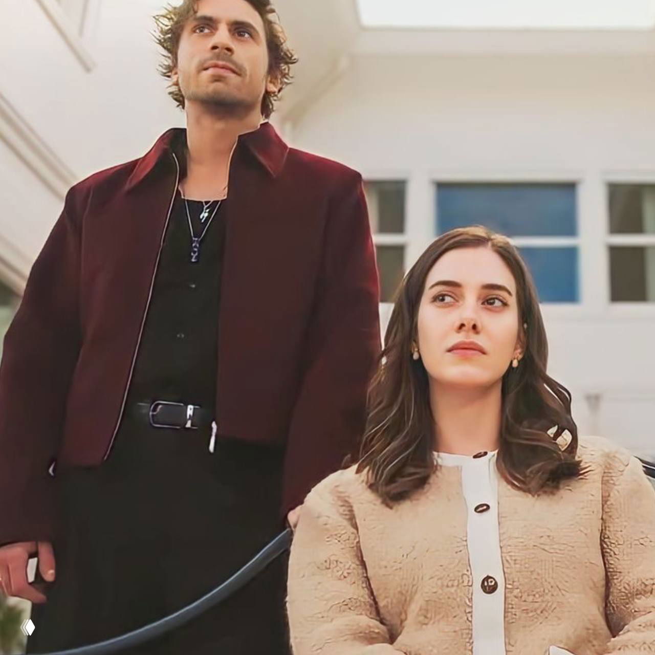 Герои стоят вместе в светлом интерьере, женщина сидит, мужчина рядом стоит вертикально — композиция подчёркивает контраст ролей и эмоций.