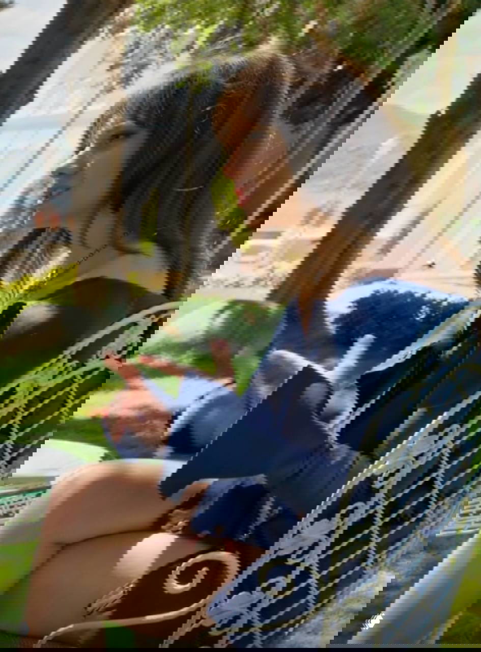 Героиня в синем открытом платье на улице у отеля: насыщенный синий на фоне зелени и пастельных фасадов.