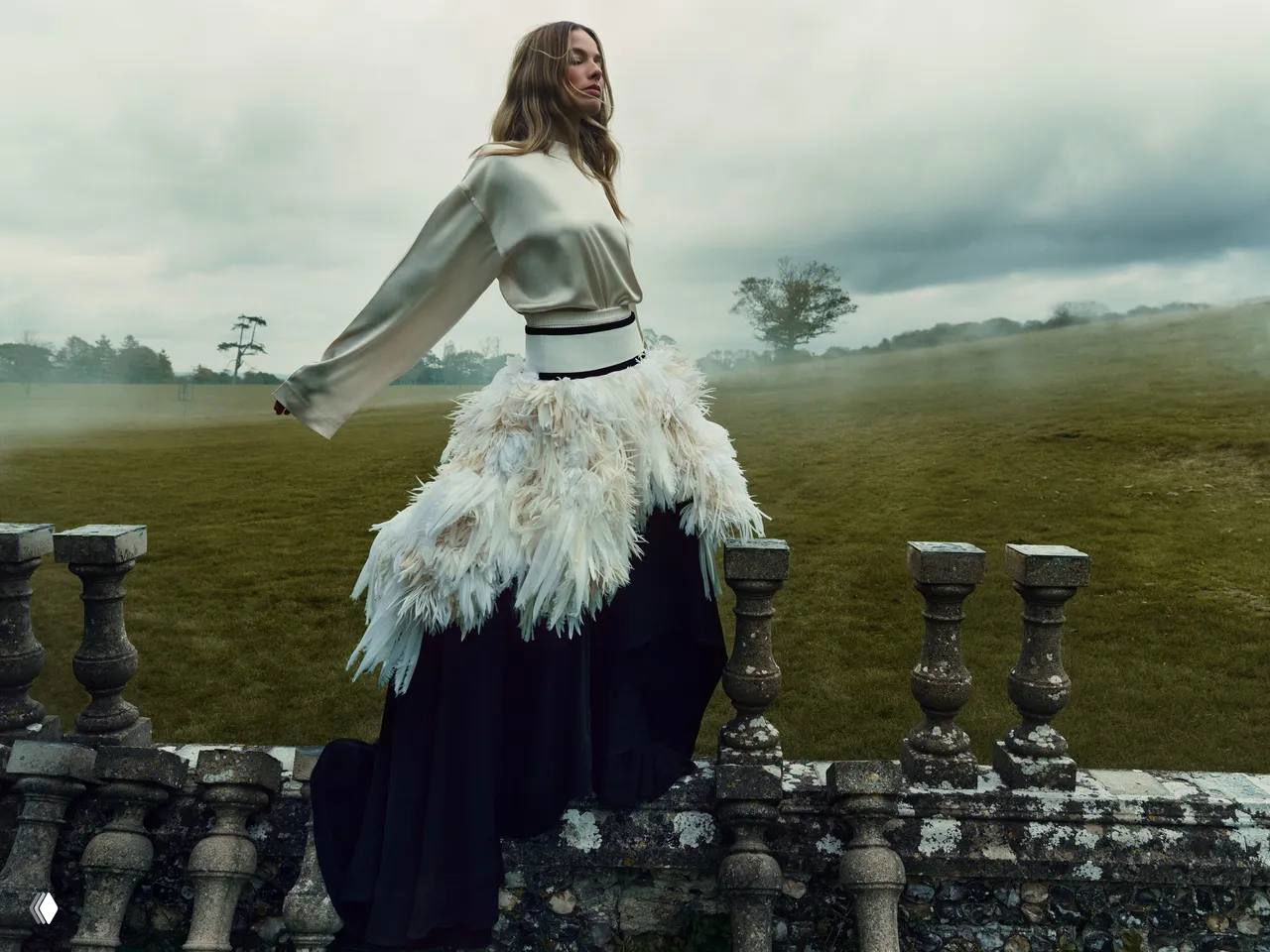 Фигура женщины в пышной юбке на фоне туманного поля и старинной ограды; атмосферная фотосессия в натуре с драматичным небом.