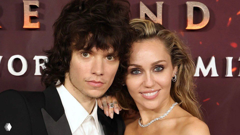 Пара на красной дорожке премьеры: мужчина в смокинге и женщина в вечернем платье позируют вместе, видны украшения и фон премьеры.