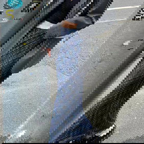 Уличный кадр образа Фрэнки из Monster High: пиджак и длинная клетчатая юбка, тёмные аксессуары на фоне городского тротуара и столба.