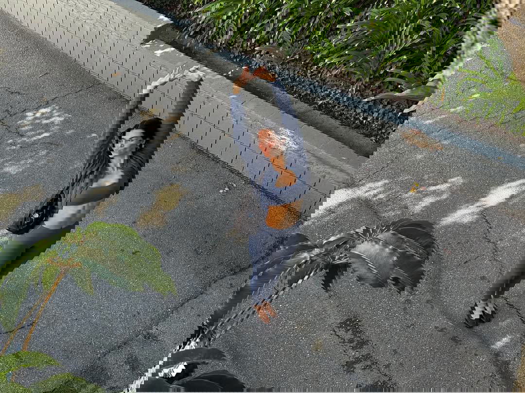 Над головой снятая фотография женщины в тёмно‑синем спортивном комплекте на улице у бордюра, она тянет руки вверх и демонстрирует фигуру и осанку.