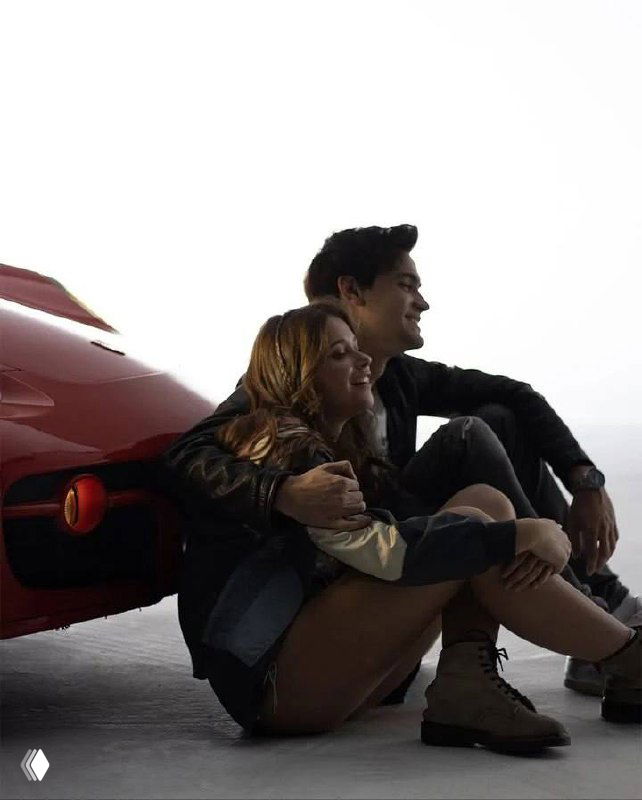 Николь Уоллес и Габриэль Гевара сидят рядом у красного автомобиля на съемочной площадке — студийный кадр с актёрами в повседневных образах.