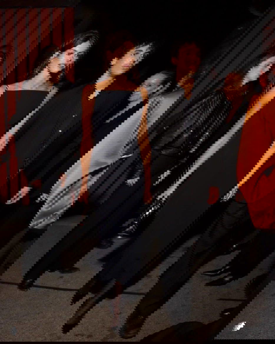 Пара знаменитых гостей в строгих тёмных образах выходит вместе после мероприятия, вечерний городской фон и люди вокруг.