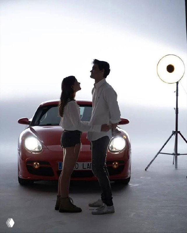 Силуэтная сцена: пара стоит перед красным автомобилем в студии с ярким задним светом и софитом, создавая романтичный силуэтный образ.
