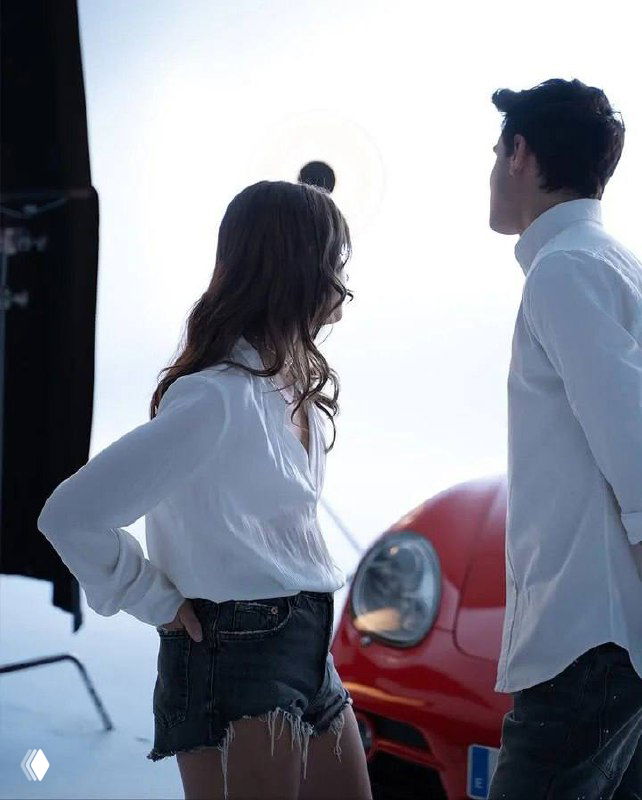 Николь и Габриэль в белых рубашках на фоне красного автомобиля — снимок на съемочной площадке, подчёркивающий стилизацию и костюмы героев.