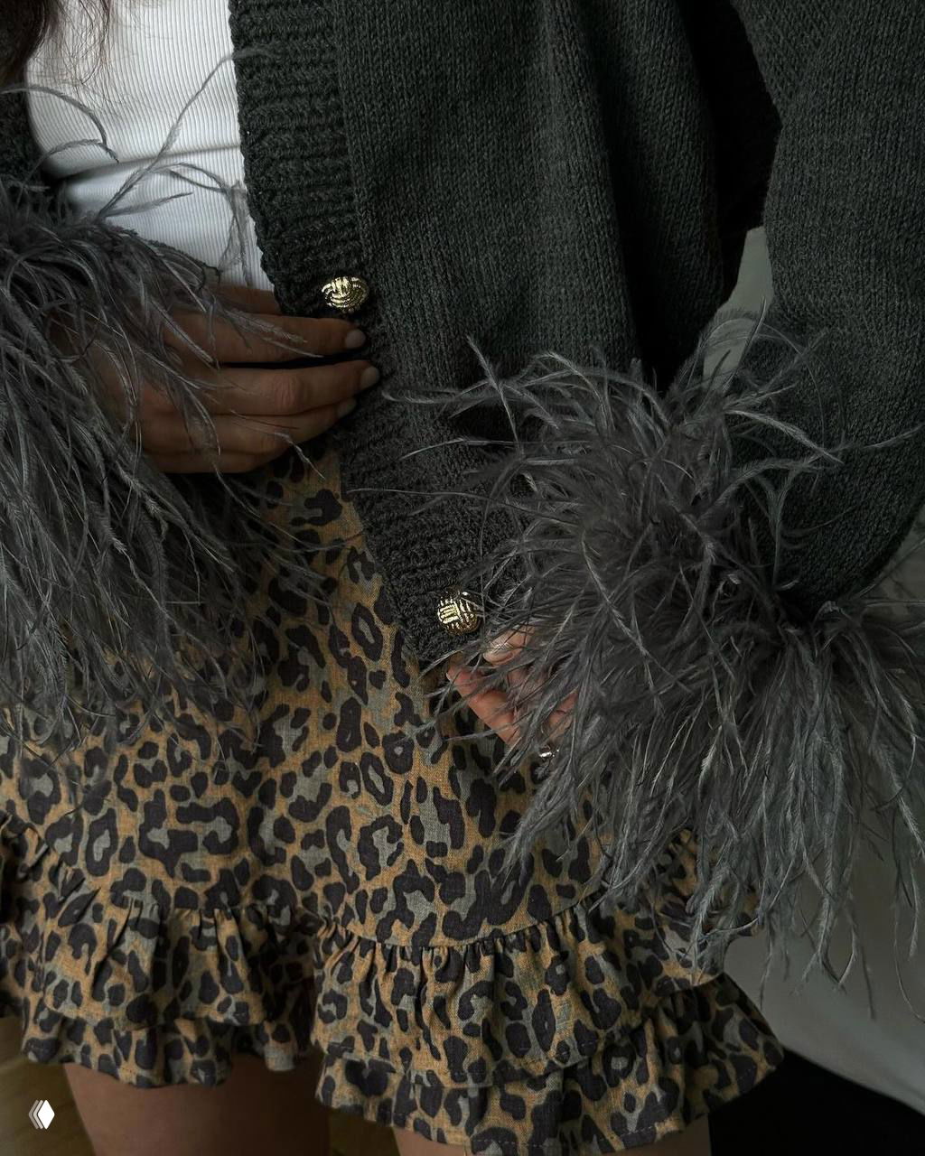 Крупный план кардигана с перьевыми манжетами и леопардовой мини-юбки — видны текстуры ткани, пуговицы и праздничная фактура образа.