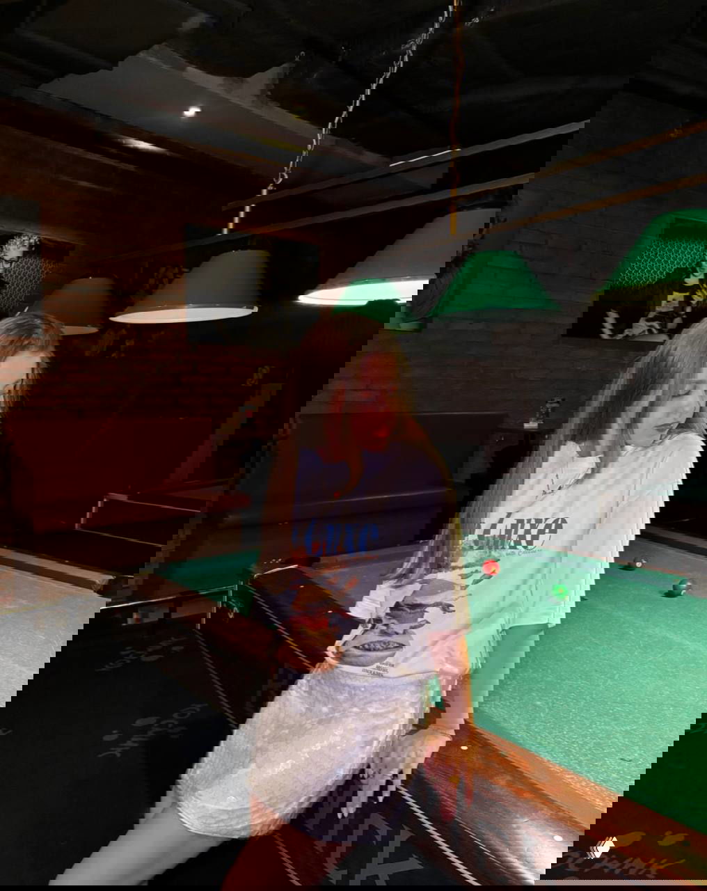 Девушка у бильярдного стола в свободной футболке и блестящей мини-юбке в пайетках — неформальный праздничный образ с игривой подачей.