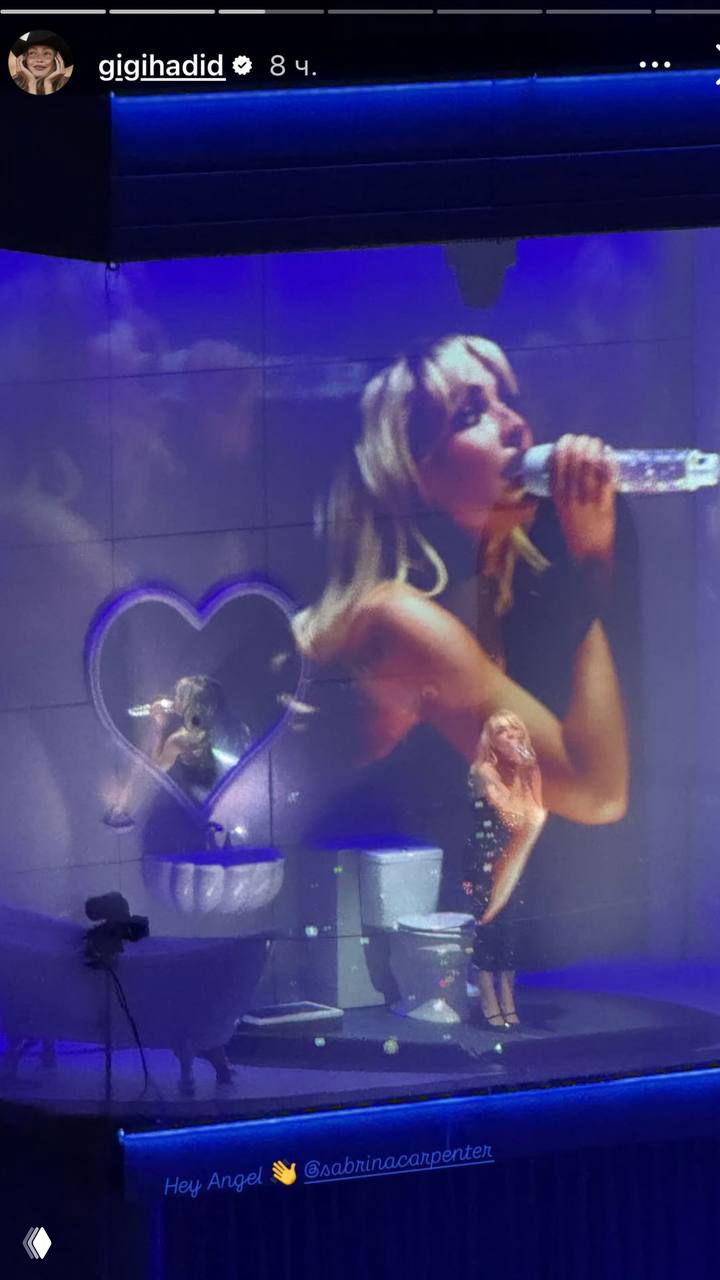 Женщина на сцене в пурпурном свете с крупной видеопроекцией на заднике; виден сценический реквизит в виде сердца и кресло, атмосферное шоу.