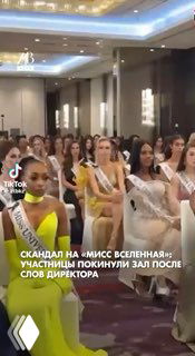 Участницы конкурса «Мисс Вселенная» в зале стоят и покидают помещение после конфликта; видны вечерние платья и обеспокоенные лица конкурсанток.
