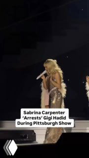 Артистка в блестящем костюме поёт в микрофон на сцене во время шоу; тёмный зал и сценическое освещение, кадр сделан из зрительного ракурса.