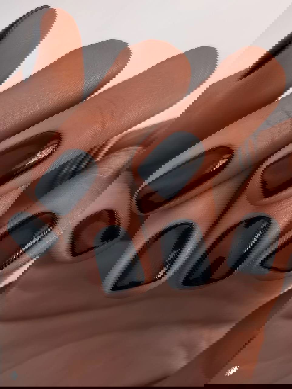 Крупный план коротких квадратных ногтей с глянцевым чёрным покрытием на фоне кожи — минималистичный тёмный маникюр.