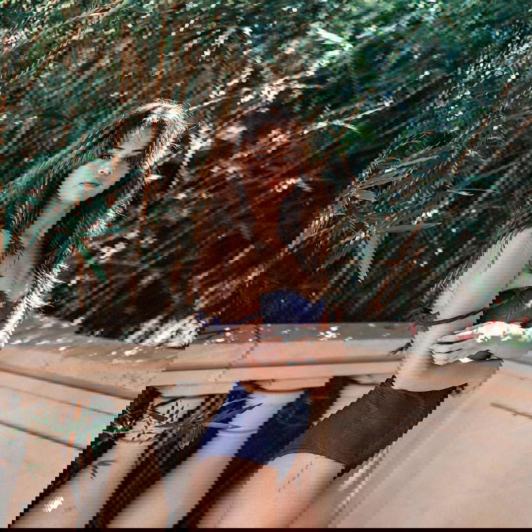 Женщина на балюстраде в синем купальнике на фоне густой зелёной растительности, естественное солнечное освещение и летняя атмосфера.