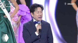 Ведущий или директор конкурса выступает на сцене «Мисс Вселенная», держит микрофон на фоне сценического оформления и конкурсанток.