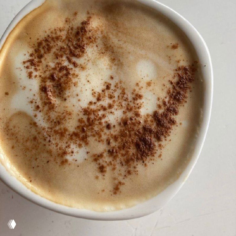 Крупный план кофейной чашки с пенкой и корицей на поверхности; тёплая кофейная текстура в бежево‑коричневой гамме