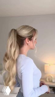 Боковой профиль молодой женщины с длинными светлыми волосами, собранными в высокий хвост с мягкими локонами, светлый интерьер комнаты на заднем плане.