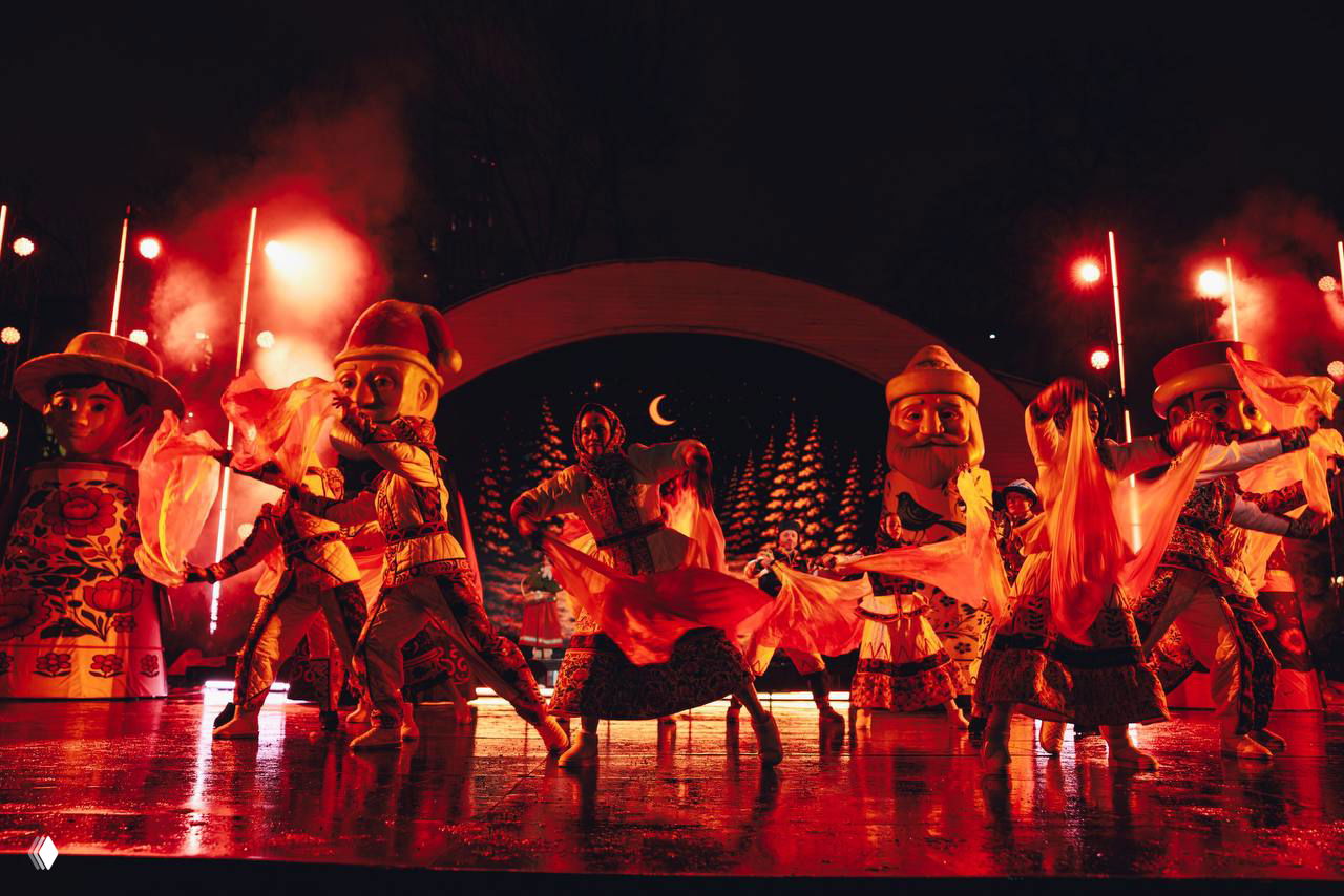 Интенсивная красная подсветка и артисты в танце на мокрой отражающейся поверхности сцены — атмосферный кадр постановки на открытом воздухе.