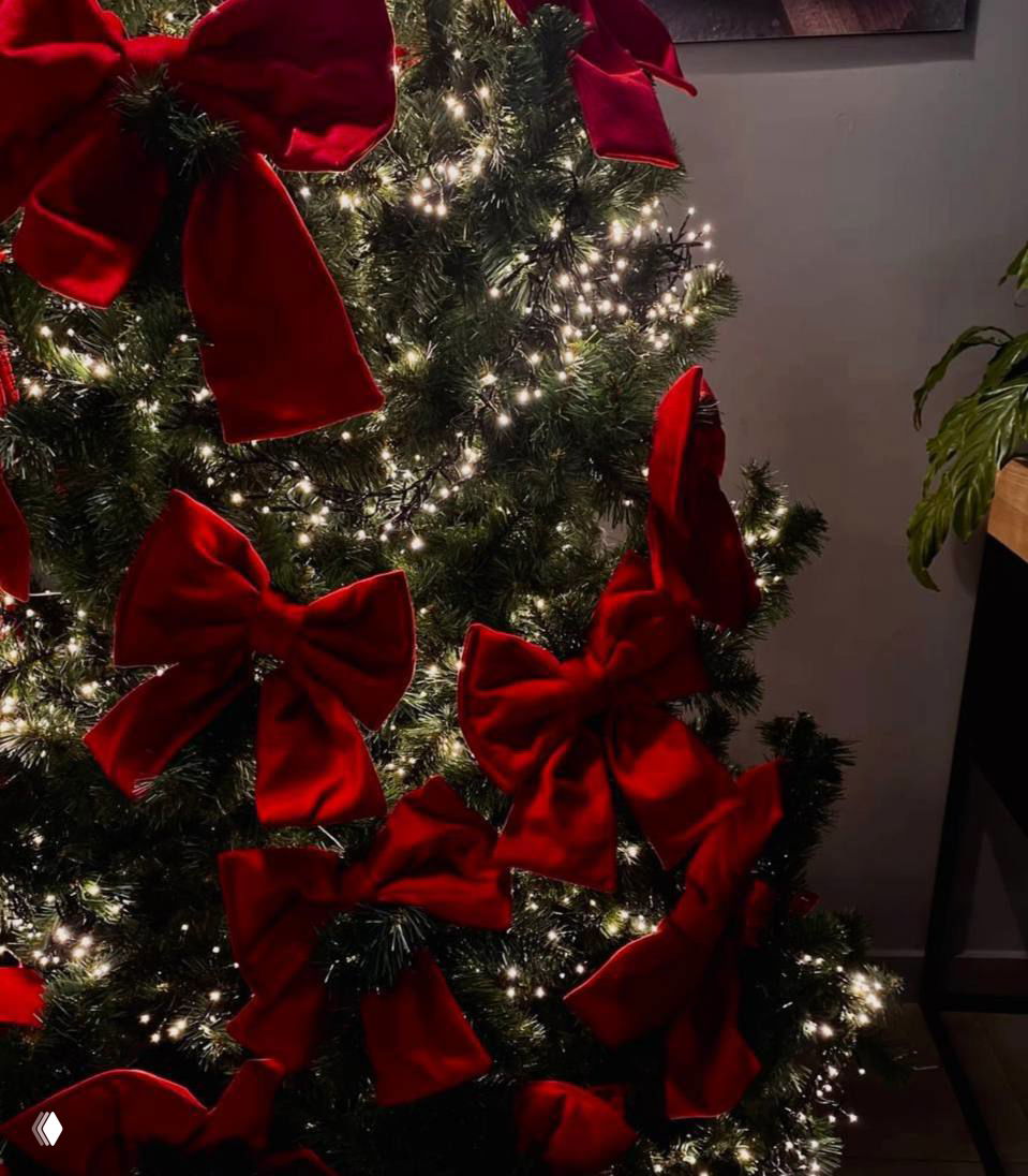 Новогодняя ёлка в интерьере с мерцающими тёплыми гирляндами и многочисленными крупными красными бантами, праздничная уютная декорация.
