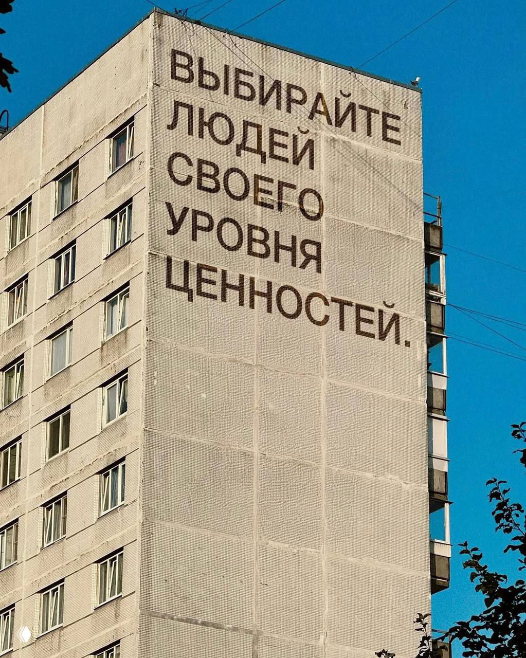 Мотивирующий текст крупными буквами на фасаде дома: призыв выбирать людей уровня своих ценностей, городской фон и ясная погода.