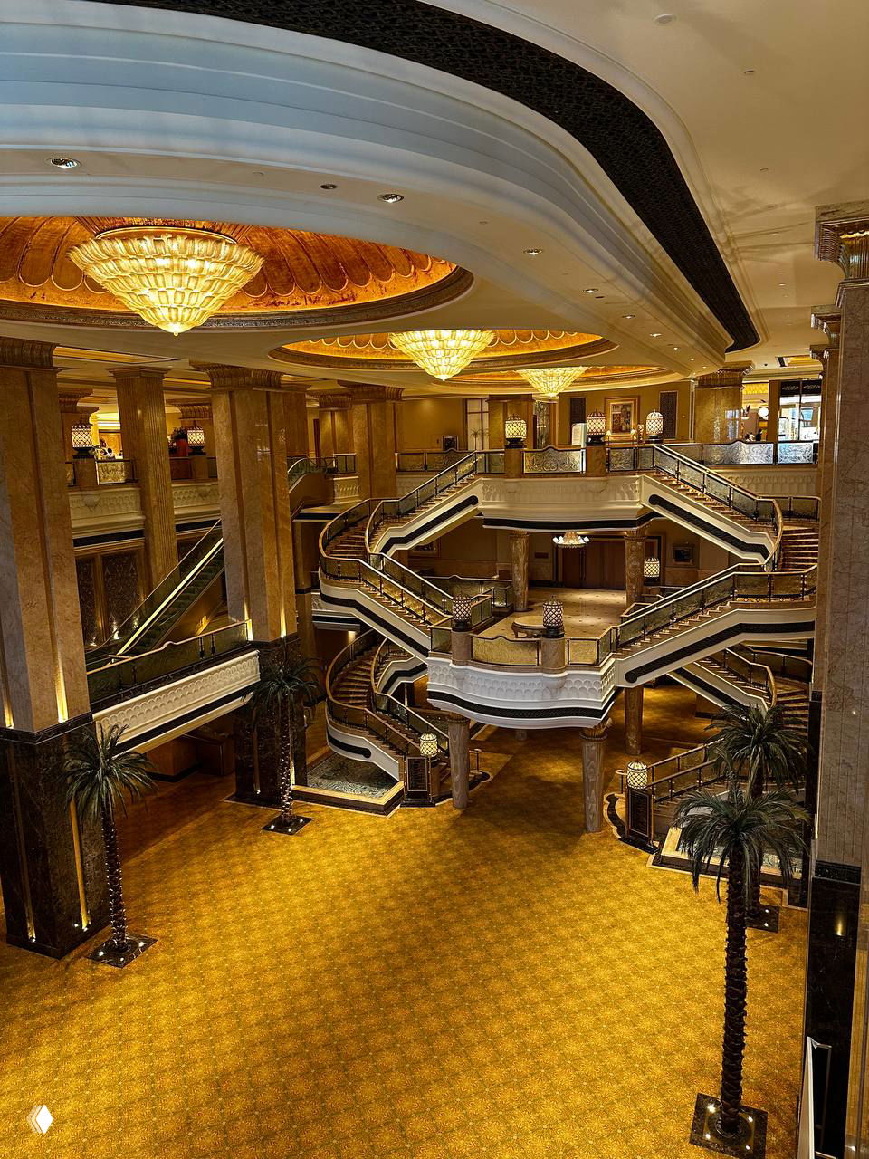 Роскошный интерьер гостиницы или торгового центра в ОАЭ: холл с мраморными колоннами, многоуровневые лестницы, большие люстры и золотистая отделка.