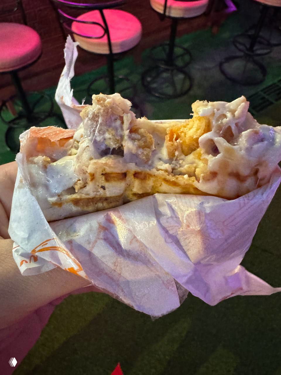 Фрагмент французского тако в бумажной обёртке: видна начинка с картофелем фри, наггетсами и обильным сырным соусом в ночной обстановке рынка.