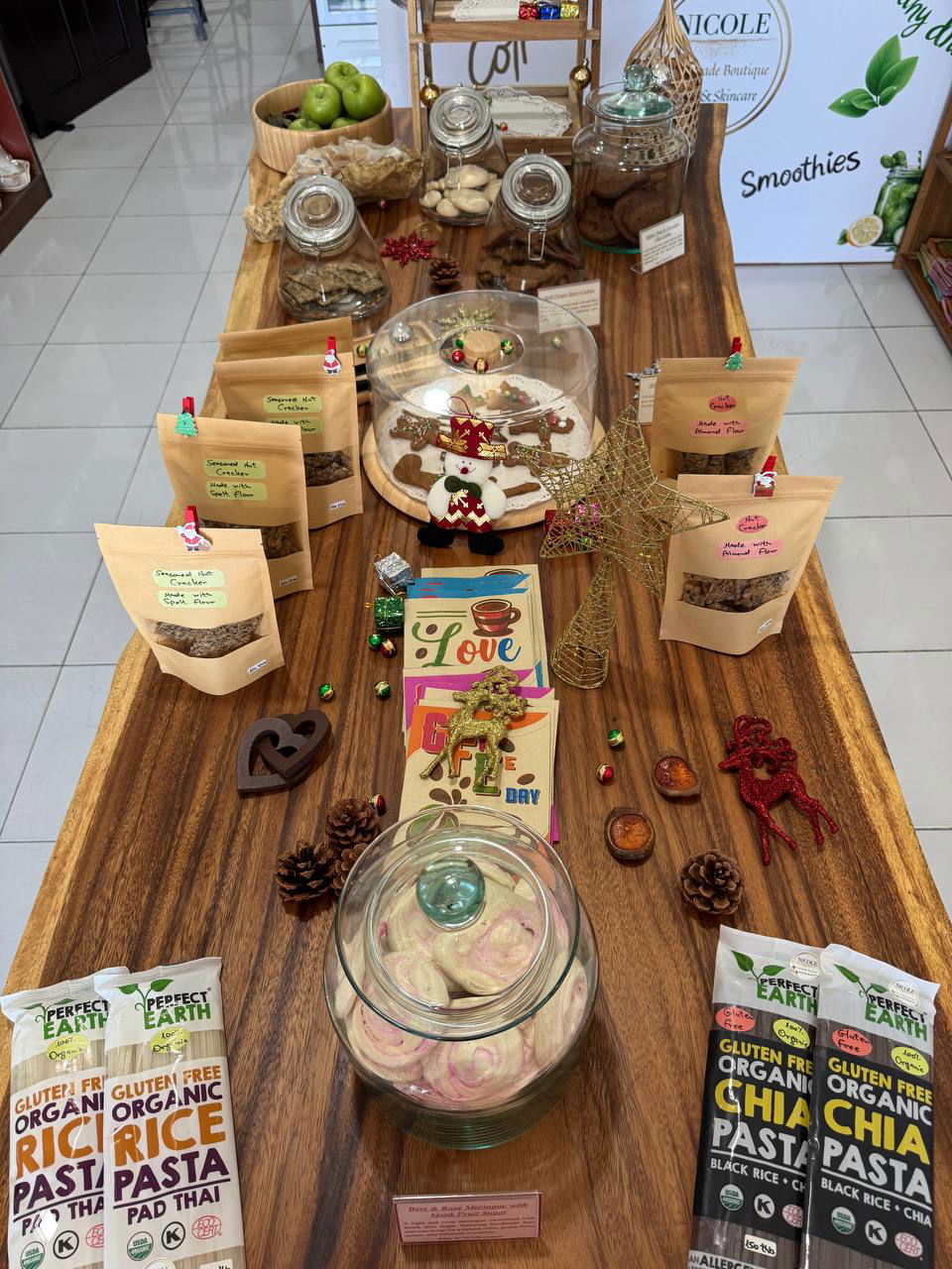 Деревянный стол с пакетиками органических продуктов, банками печенья и стеклянной банкой с меренгами — стилизованная витрина с угощениями.