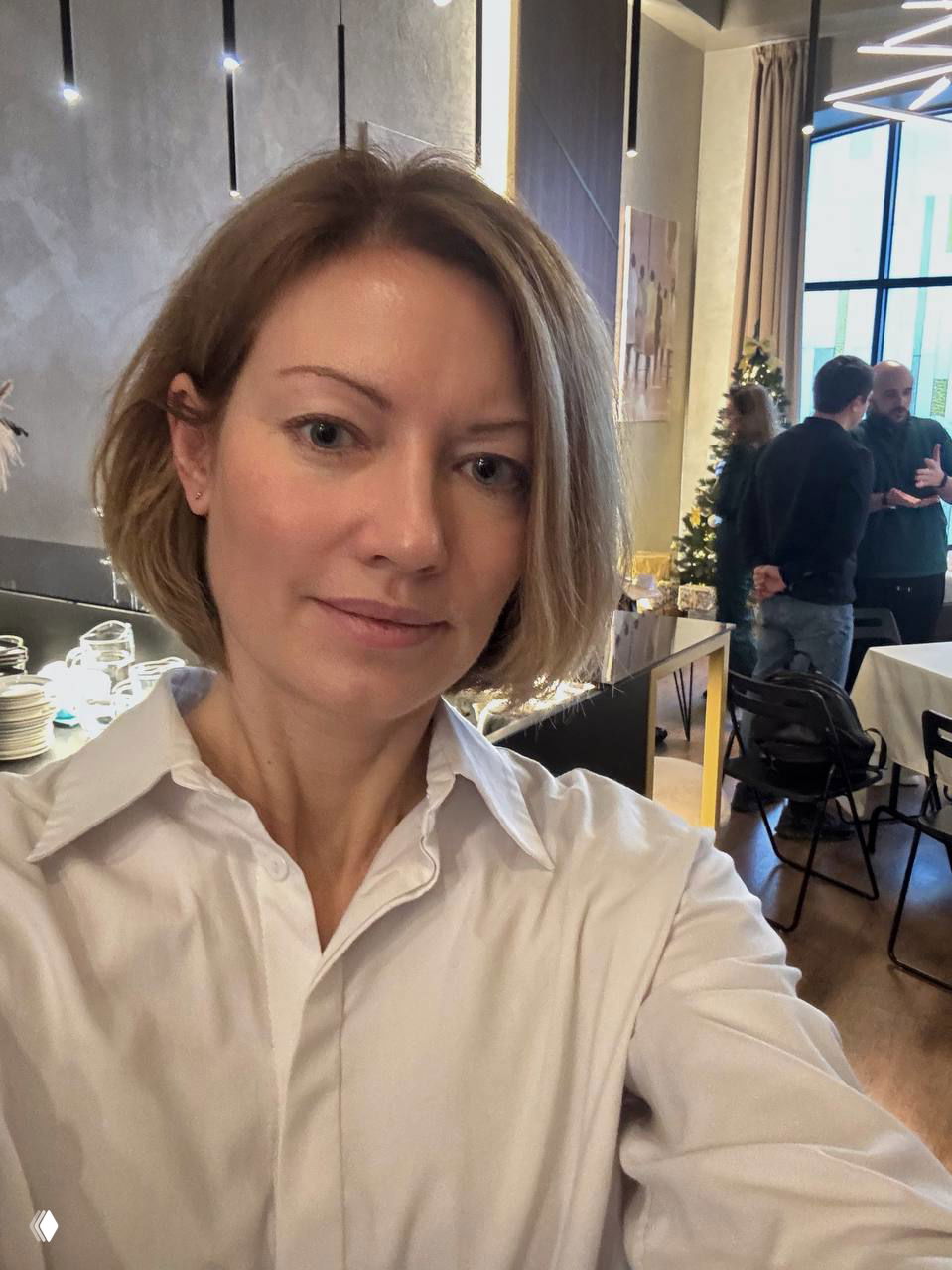 Селфи автора на фоне зоны мероприятия для собственников клиник: сервировка столов, посуда и люди на заднем плане в комнате встречи.