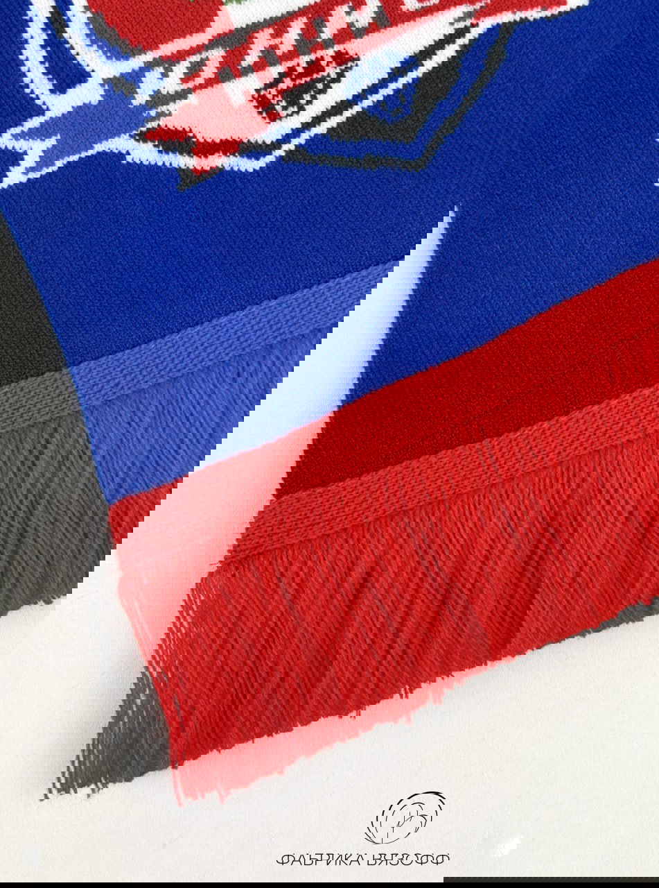 Крупный план красной бахромы и кромки вязаного шарфа на белом фоне, хорошо видна фактура пряжи и аккуратный шов изделия.