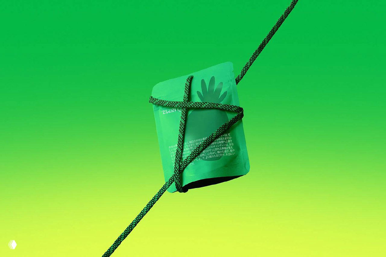 Крупный план минималистичной упаковки конфет Zzzeny на ярком зелёно‑жёлтом градиенте, с силуэтными иллюстрациями и текстурой поверхности.