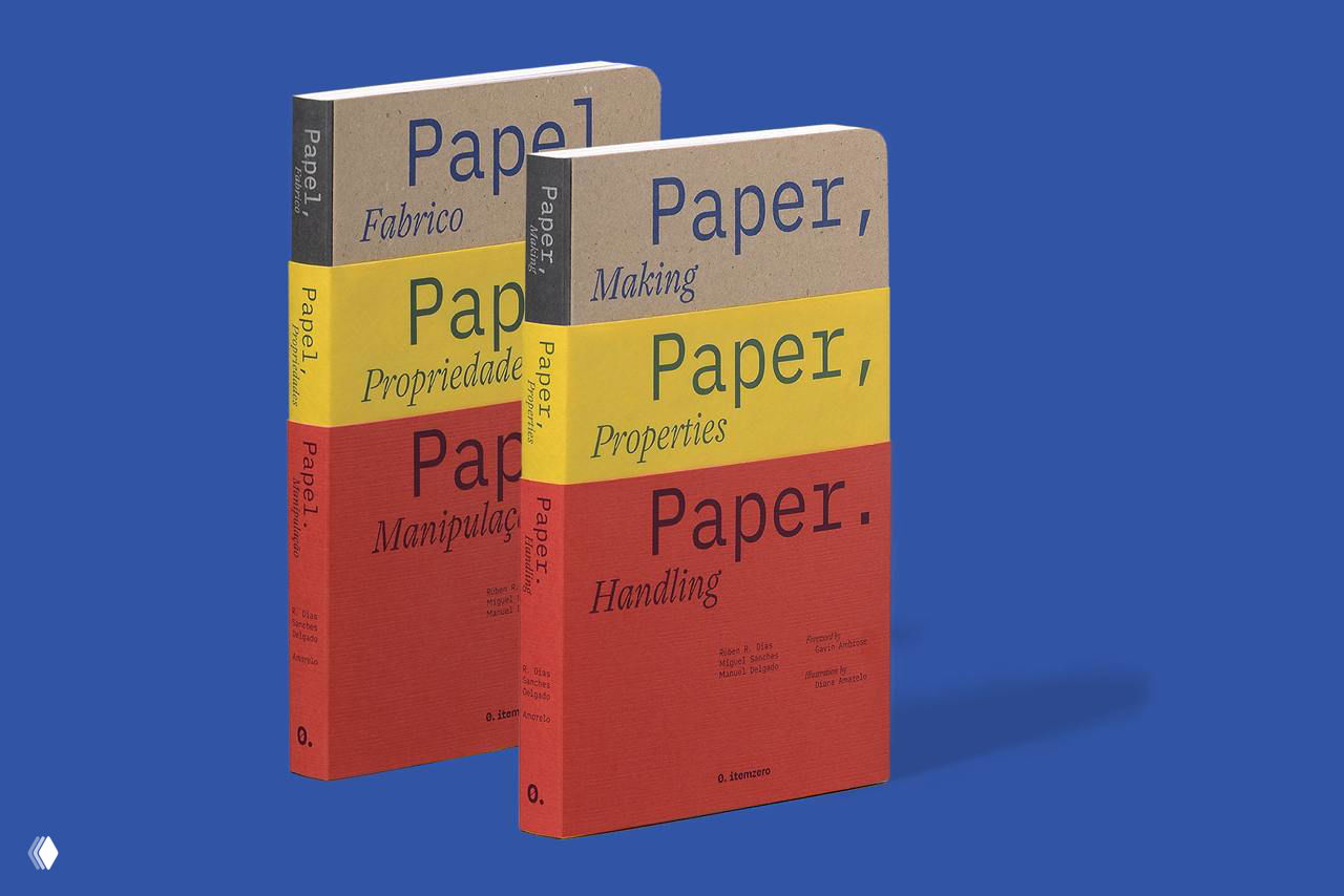 Две копии книги «Paper, Paper, Paper» в твердой фактурной обложке с желтыми и красными поясами на однотонном синем фоне, вид спереди.
