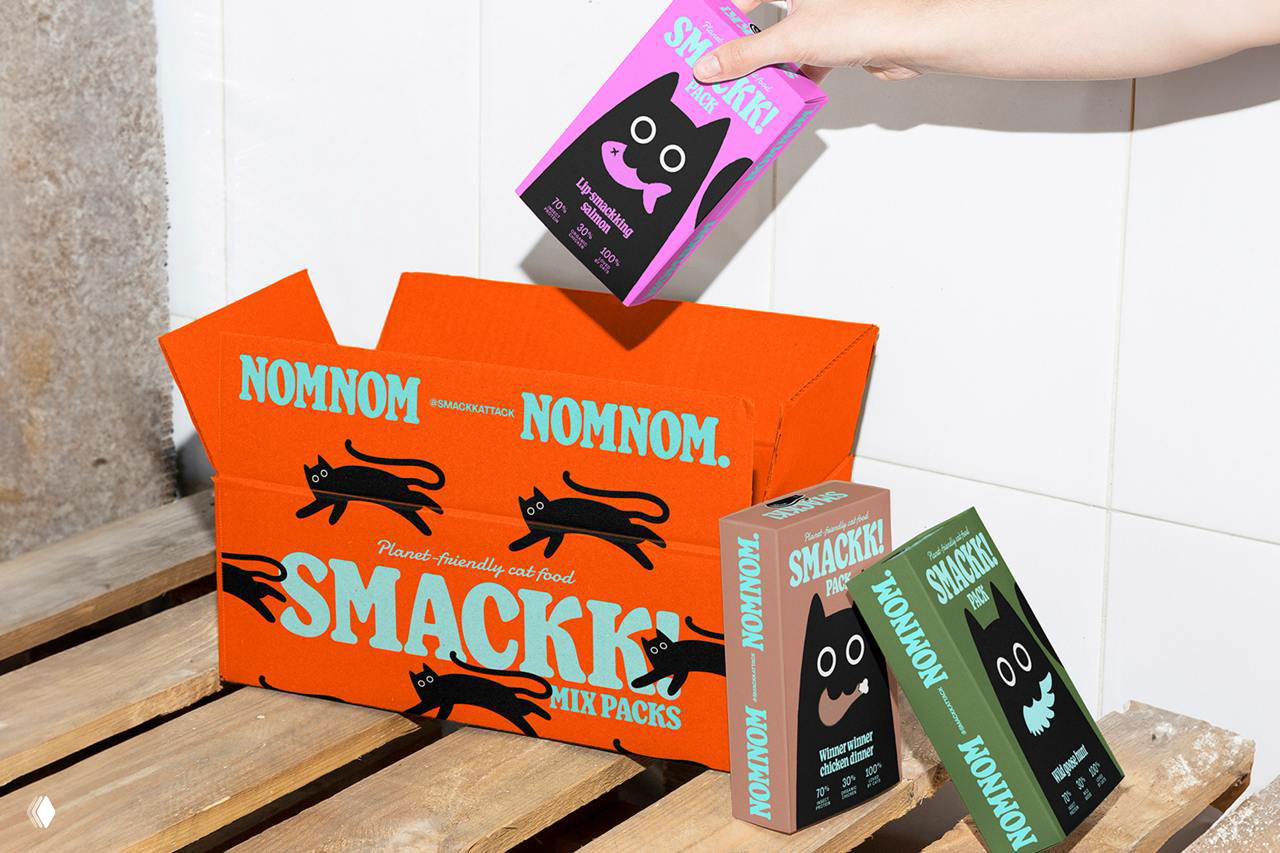 Открытая коробка Smackk с микс-паками внутри: руки держат упаковки, показаны коробки с фирменными котами и надписью NOMNOM.