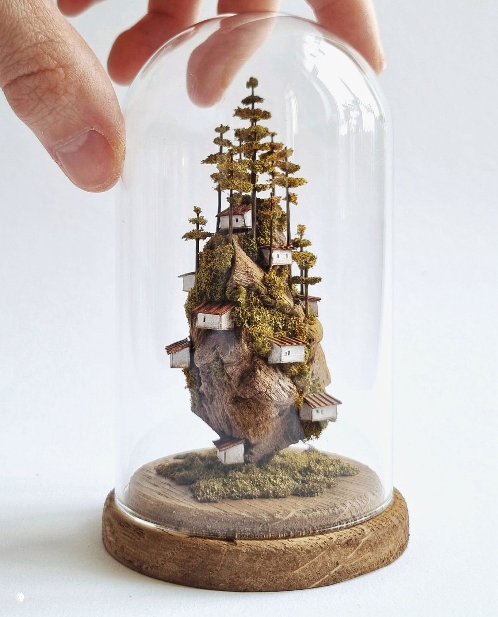 Крошечный ландшафт на деревянной подставке: каменистый остров с домиками и высокими тонкими деревьями, сфокусированный крупным планом.