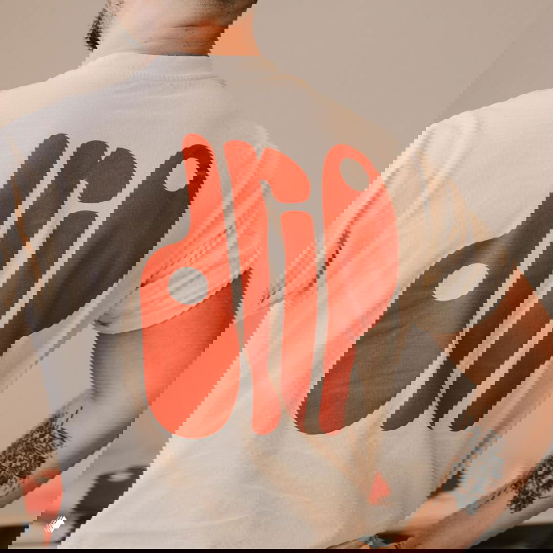 Сотрудник в футболке с крупным красным принтом логотипа Drip на спине; демонстрация мерча и графической системы бренда в одежде персонала.