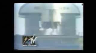 Фрагмент архивного клипа в низком разрешении: индустриальный пейзаж и стилизованный логотип MTV в углу, характерный для эфирных записей из архива.