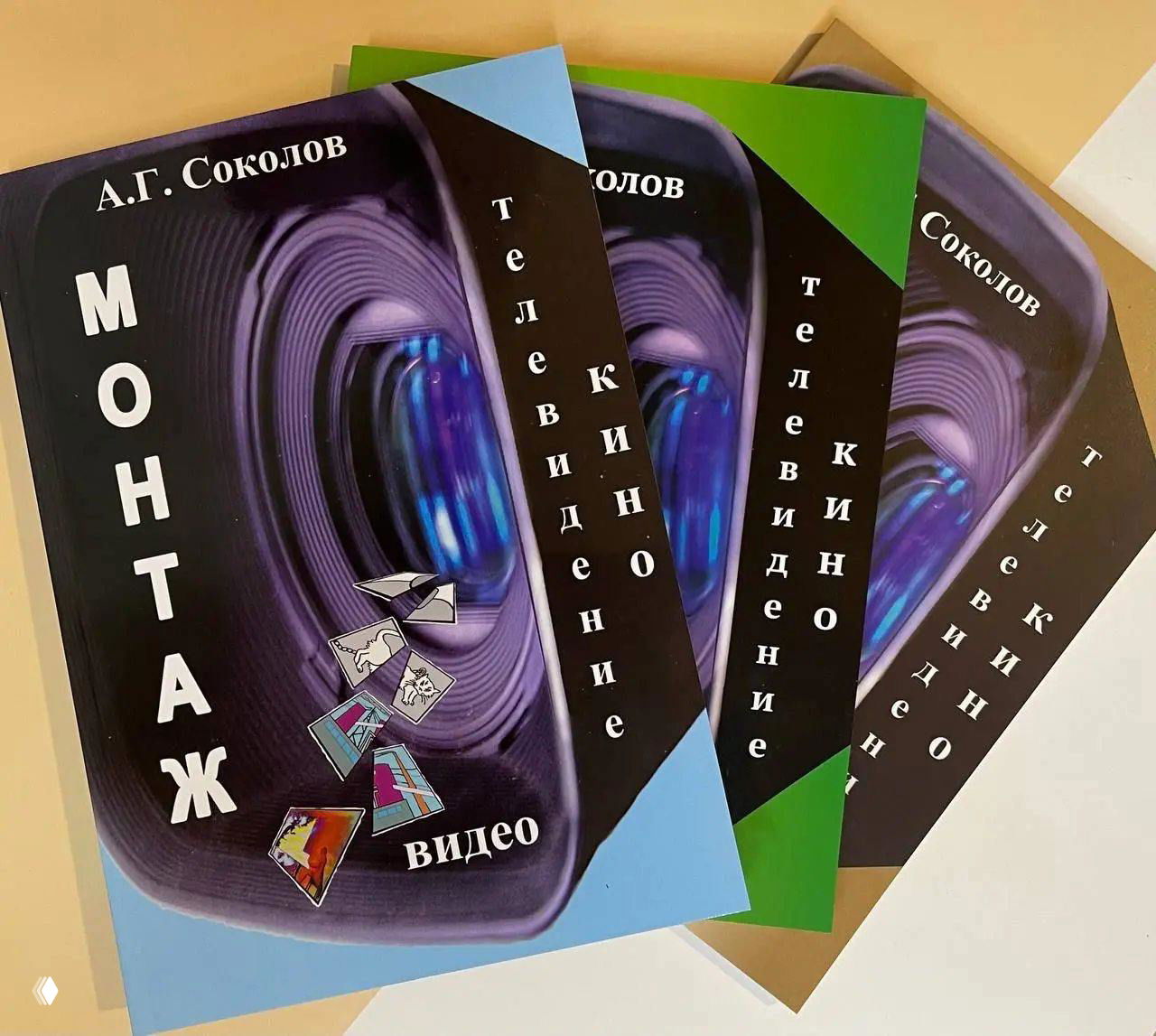 Фото обложек книги А. Г. Соколова «Монтаж: телевидение, кино, видео» — несколько экземпляров внахлёст на столе, видны иллюстрация объектива и шрифт.