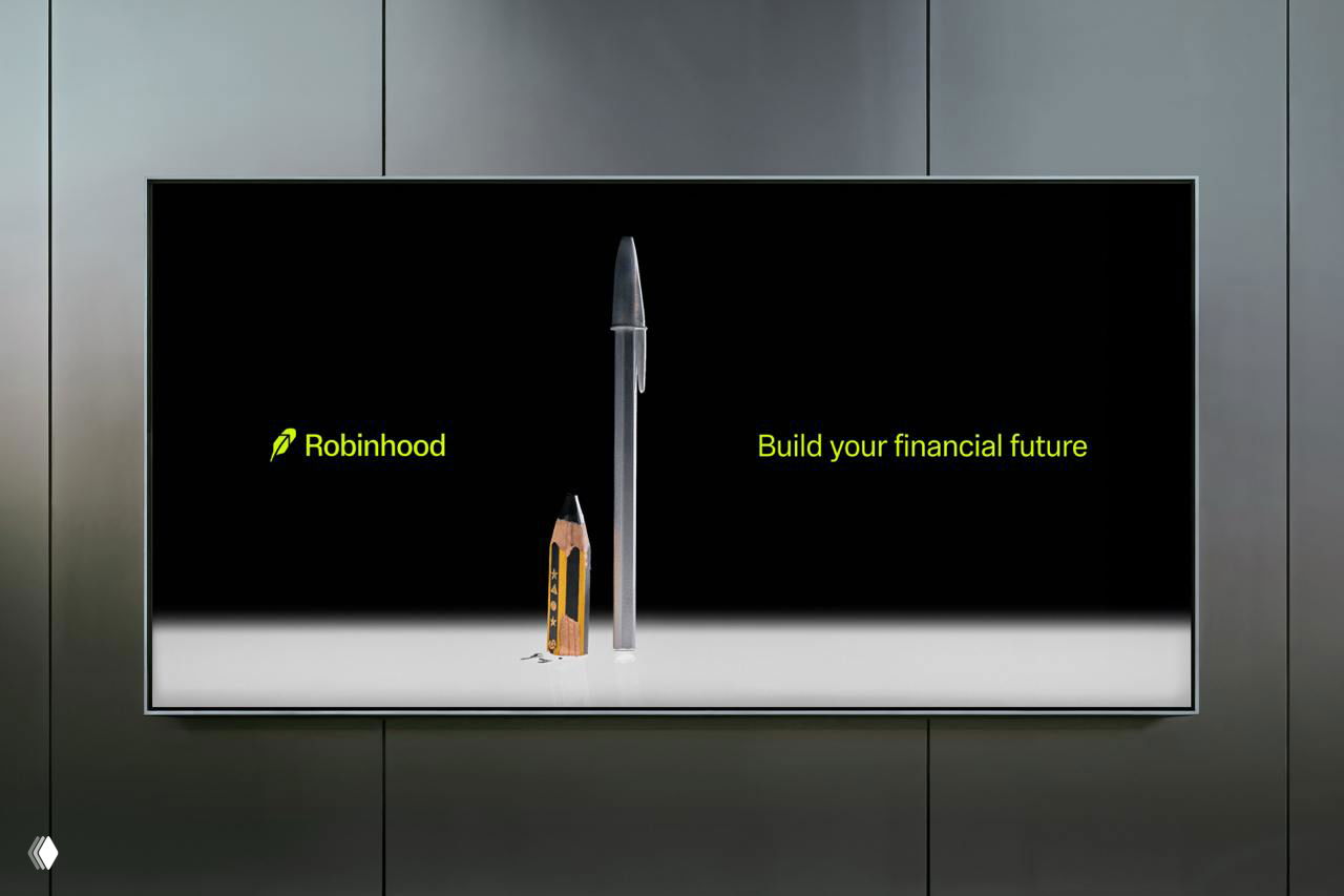 Рекламный экран с логотипом Robinhood и надписью «Build your financial future», рядом карандаш и ручка на минималистичной сцене с тёмным фоном.