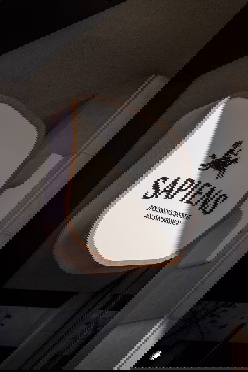 Объёмная уличная вывеска SAPIENS с логотипом всадника и надписью «SPECIALTY COFFEE & ALL DAY BRUNCH» на светлом фоне у фасада.