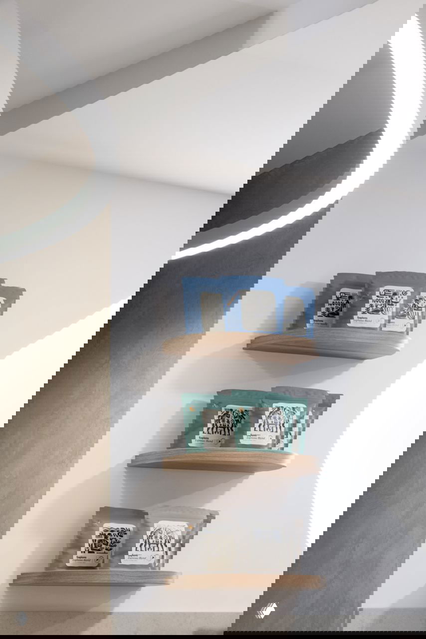 Полки с фирменными упаковками кофе Sapiens разного цвета на светлой стене — демонстрация айдентики и продуктовой линейки бренда.