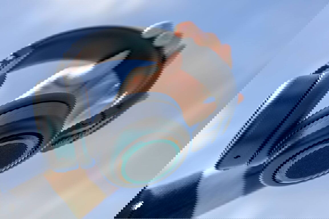 Рука держит наушники крупным планом; виден внешний динамик и конструкция с наружными и внутренними динамиками, подчёркивающая уникальную концепцию.