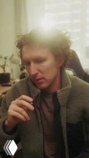 Портрет мужчины в комнате при мягком дневном свете из окна; он в тёплой одежде, задумчиво смотрит вниз, нейтральный фон.