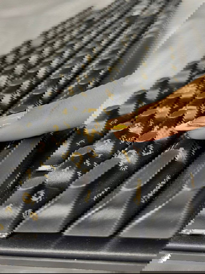 Крупный план чёрной клавиатуры DeLiz с углублёнными колпачками; палец с длинным золотым маникюром нажимает клавишу.